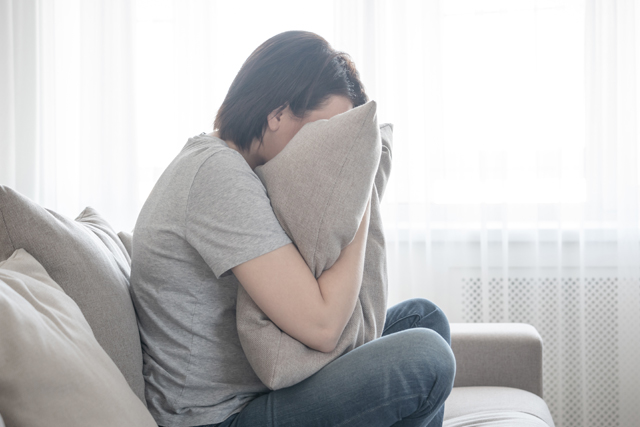 A person sitting on a couch and hugging a large pillow while hiding their face