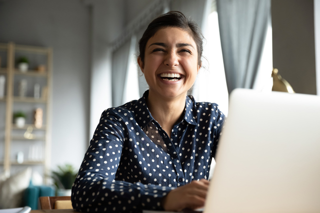 woman laughing while using laptop