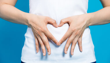 Young woman who makes a heart shape by hands on her stomach