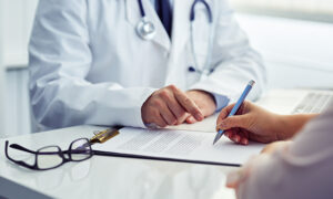 Female patient in office filling out medical document with doctor