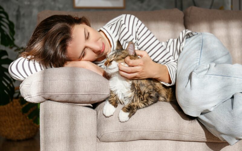 Young woman cuddling her cat at home on her couch