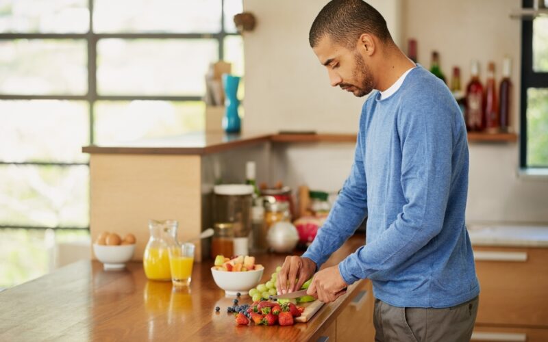 A man cutting up fruit to eat, enjoying a nutritous meal