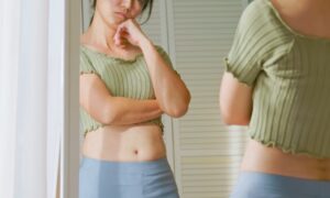 Woman standing in front of mirror unhappy with her weight