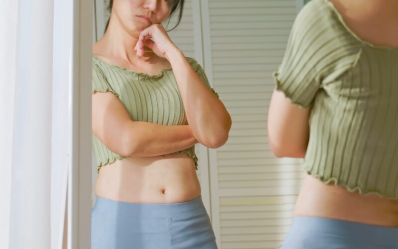 Woman standing in front of mirror unhappy with her weight