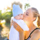 Woman holding and kissing her baby while enjoying outdoors