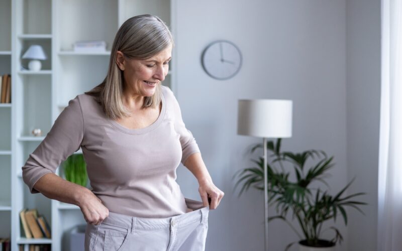 Older woman happy with her weight loss after trying on her old pants
