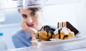 Hungry young woman looking at dessert in the fridge