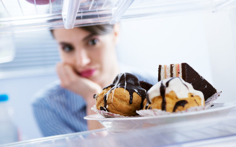 Hungry young woman looking at dessert in the fridge