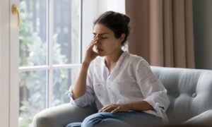 Young woman dealing with headache while sitting on couch