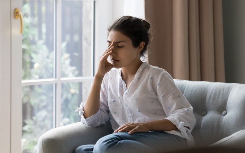 Young woman dealing with headache while sitting on couch