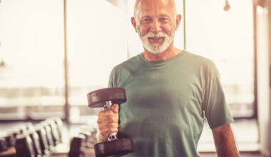 Smiling older man in the gym holding a dumbbell