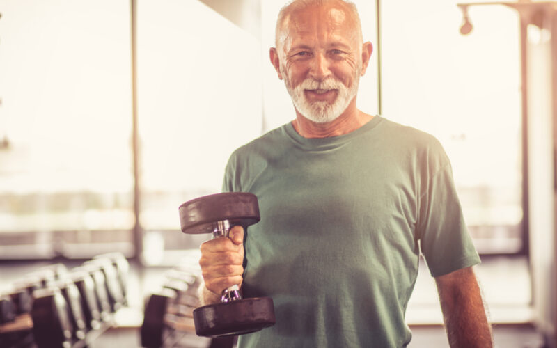 Smiling older man in the gym holding a dumbbell