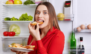 Young hungry woman eating in front of open fridge