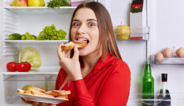 Young hungry woman eating in front of open fridge