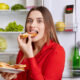 Young hungry woman eating in front of open fridge