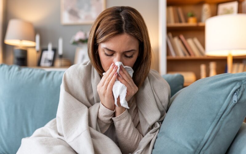 Young woman blowing her nose and dealing with sickness