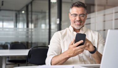 Middle aged man smiling at phone while sitting at office desk