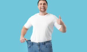 Young man happy as he shows weight loss with his old pants