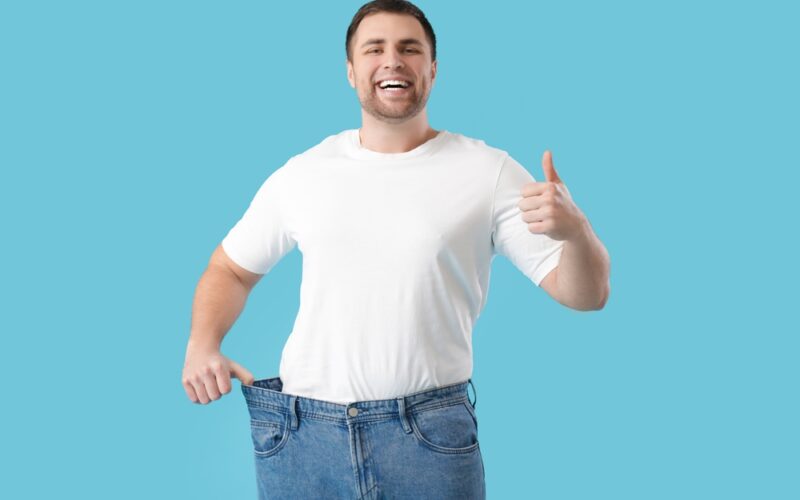 Young man happy as he shows weight loss with his old pants