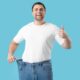 Young man happy as he shows weight loss with his old pants