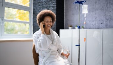 Woman sitting down on the phone with a glass of water while getting IV therapy