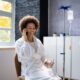 Woman sitting down on the phone with a glass of water while getting IV therapy
