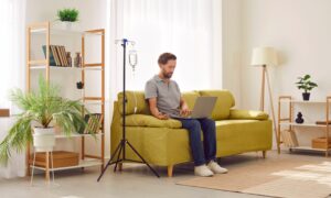 Man receiving IV therapy while sitting on couch with his laptop