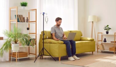 Man receiving IV therapy while sitting on couch with his laptop