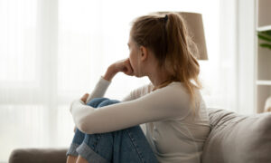 Side view of unhappy woman looking into the distance, sitting on the couch