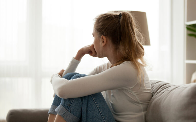 Side view of unhappy woman looking into the distance, sitting on the couch