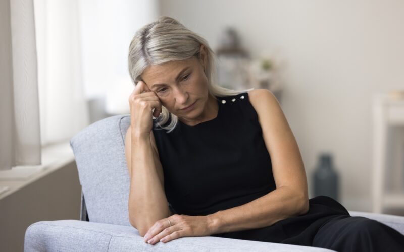 Unhappy middle aged woman sitting on couch