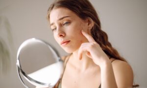 Woman looking at her skin and acne in a small mirror