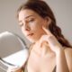 Woman looking at her skin and acne in a small mirror