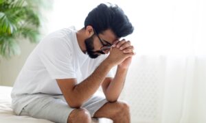 Upset man sitting at edge of the bed with head in his hands