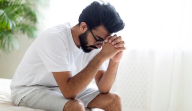 Upset man sitting at edge of the bed with head in his hands