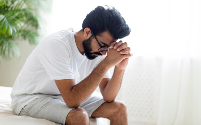 Upset man sitting at edge of the bed with head in his hands