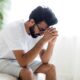 Upset man sitting at edge of the bed with head in his hands