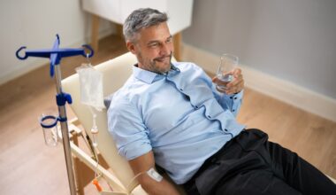 Man laying back receiving vitamin IV therapy and holding a glass of water