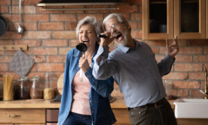 Older couple in their kitchen using kitchen utensils as microphones and singing