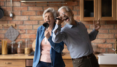 Older couple in their kitchen using kitchen utensils as microphones and singing