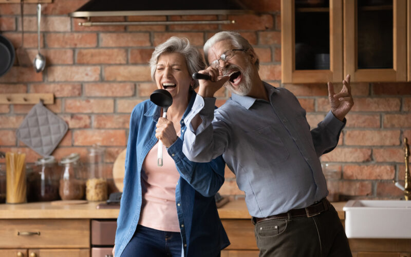 Older couple in their kitchen using kitchen utensils as microphones and singing
