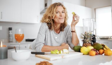 Woman smiling at camera while eating fruits in the kitchen