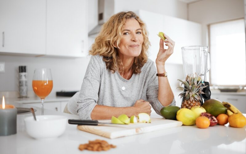 Woman smiling at camera while eating fruits in the kitchen