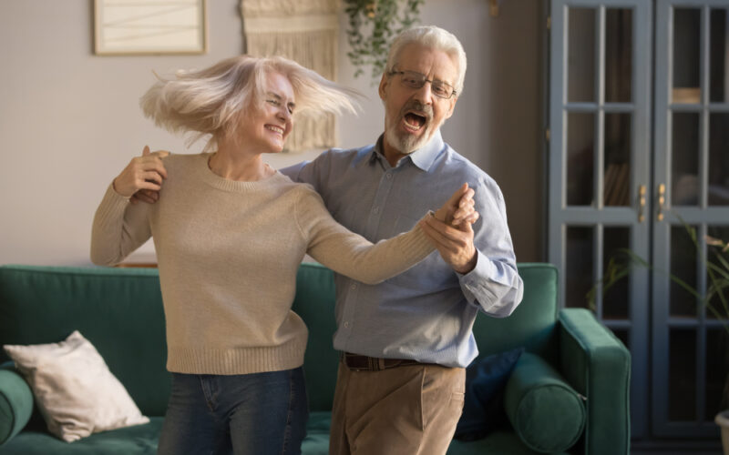 Happy and active older couple dancing in their living room