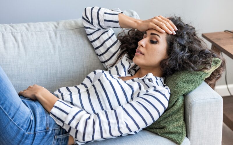 Woman laying down on the couch, stressed out and deep in thought
