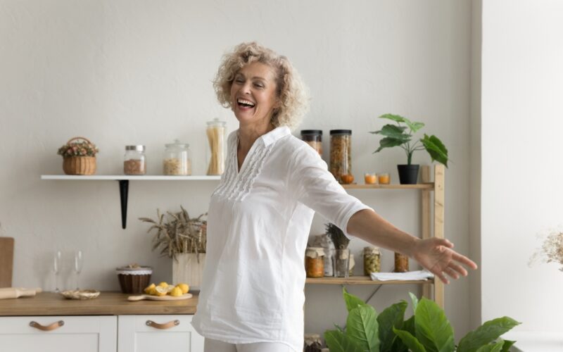 Happy and cheerful older woman having fun at home and smiling with arms out