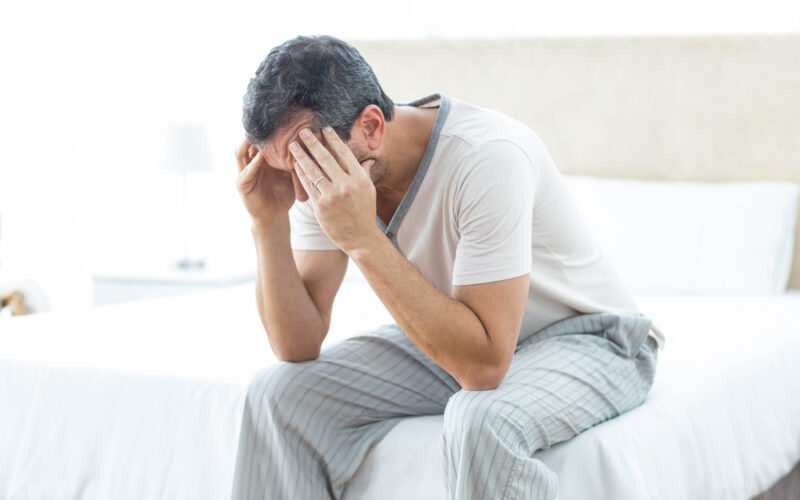 Close up of man upset, sitting on the edge of his bed with his head in his hands