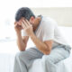 Close up of man upset, sitting on the edge of his bed with his head in his hands