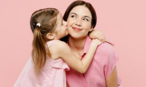 A young girl hugging an adult woman, both wearing pink, against a pink background.