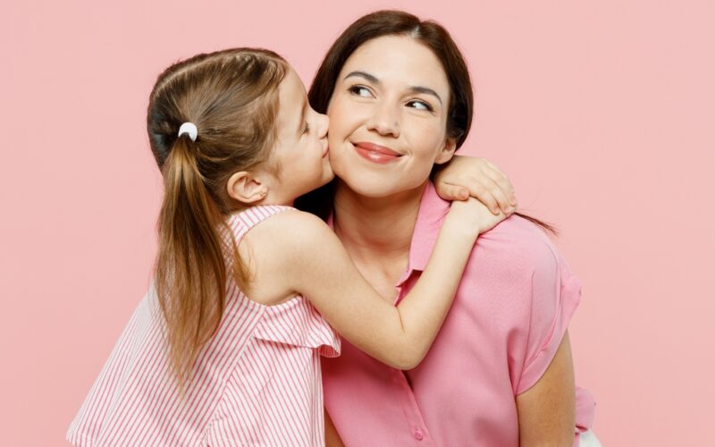 A young girl hugging an adult woman, both wearing pink, against a pink background.